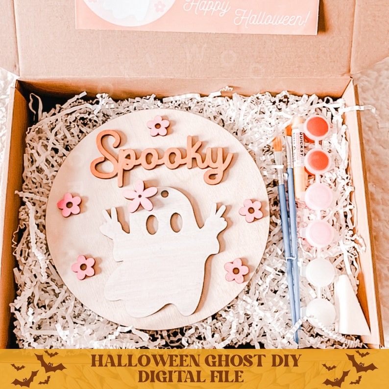 May include: A DIY Halloween ghost craft kit with a wooden circle, paint, brushes, and pink flowers. The circle has the word "Spooky" and a ghost with peace signs.