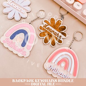 May include: A set of three wooden keychains featuring rainbow designs with the names "Mikaela" and "Leonare" in a cursive font. The keychains are attached to silver key rings.