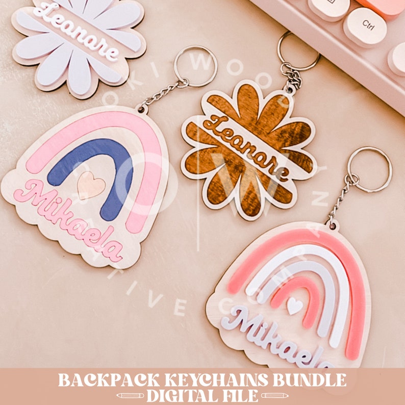 May include: A set of three wooden keychains featuring rainbow designs with the names "Mikaela" and "Leonare" in a cursive font. The keychains are attached to silver key rings.
