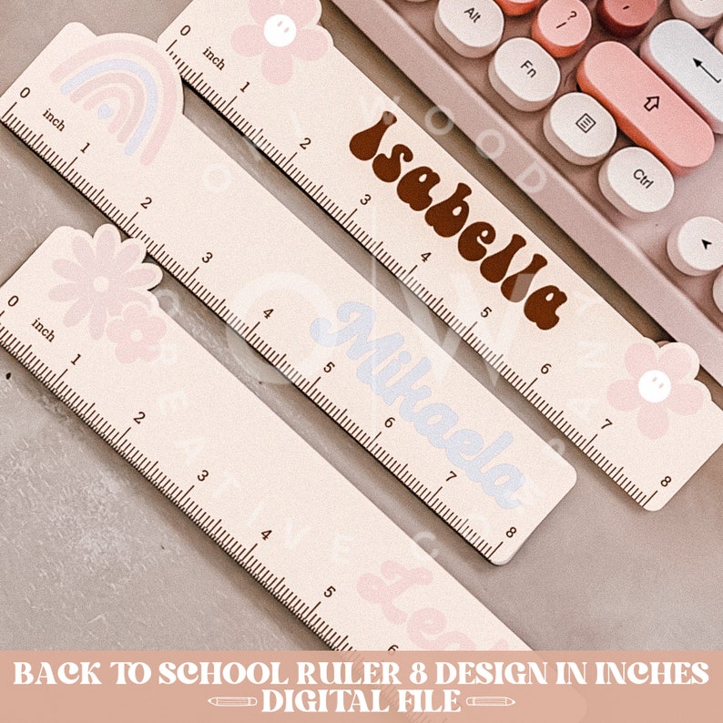 May include: Set of eight personalized rulers with a pastel pink and white background. Each ruler features a different design, including a rainbow, a flower, and a smiley face. The rulers are labeled with the names "Isabella", "Mikaela", and "Leo".