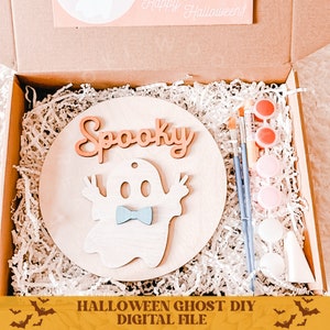May include: A wooden craft kit with a ghost cutout, the word "Spooky" and paint supplies. The kit is in a brown box with white shredded paper.