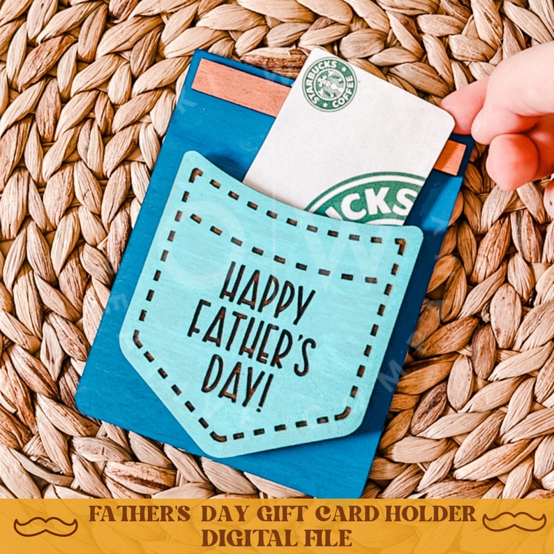 May include: A blue wooden gift card holder with a pocket for a gift card. The pocket is cut out in the shape of a pocket and has the text "Happy Father's Day!" on it. The holder is sitting on a woven straw surface.