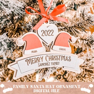 Puede incluir: Un adorno navide&ntilde;o de madera con dos gorros de Pap&aacute; Noel, un coraz&oacute;n con el a&ntilde;o 2022 y una pancarta que dice "Feliz Navidad Familia Sanchez".