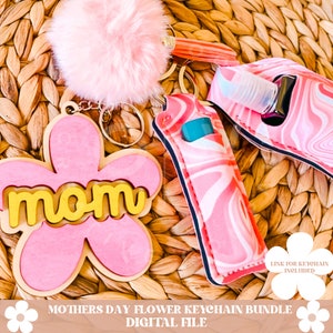 Puede incluir: Llavero de flor rosa y amarillo con la palabra "mom" en &eacute;l. El llavero tambi&eacute;n incluye un porta b&aacute;lsamo labial marmoleado rosa y blanco y un pomp&oacute;n rosa peludo.  Paquete de llavero de flor del D&iacute;a de la Madre Archivo digital.