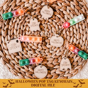 Op de afbeelding: Een set van zes Halloween-thema pop-it sleutelhangers. De tags zijn gemaakt van hout en hebben verschillende ontwerpen, waaronder geesten, pompoenen en de tekst "Stay Spooky!" en "Happy Halloween!"