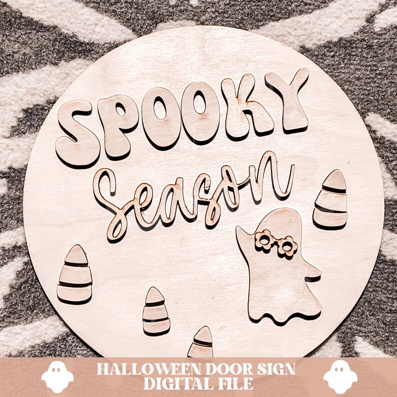 Peut inclure: Une pancarte ronde en bois avec le texte "Spooky Season" dans une police de caract&egrave;res fantaisiste. La pancarte repr&eacute;sente un fant&ocirc;me avec un bandeau et des d&eacute;corations de ma&iuml;s sucr&eacute;.