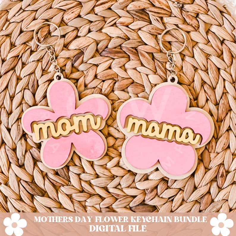 Puede incluir: Dos llaveros en forma de flor rosa con letras doradas. Un llavero dice "mom" y el otro dice "mama".