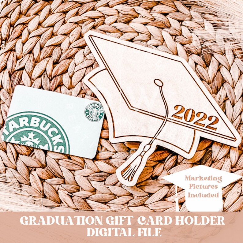 May include: A wooden graduation cap cutout with the year 2022 engraved on it. The cap is designed to hold a gift card. The image includes a Starbucks gift card as an example.  The text "Marketing Pictures Included" is also visible in the image.