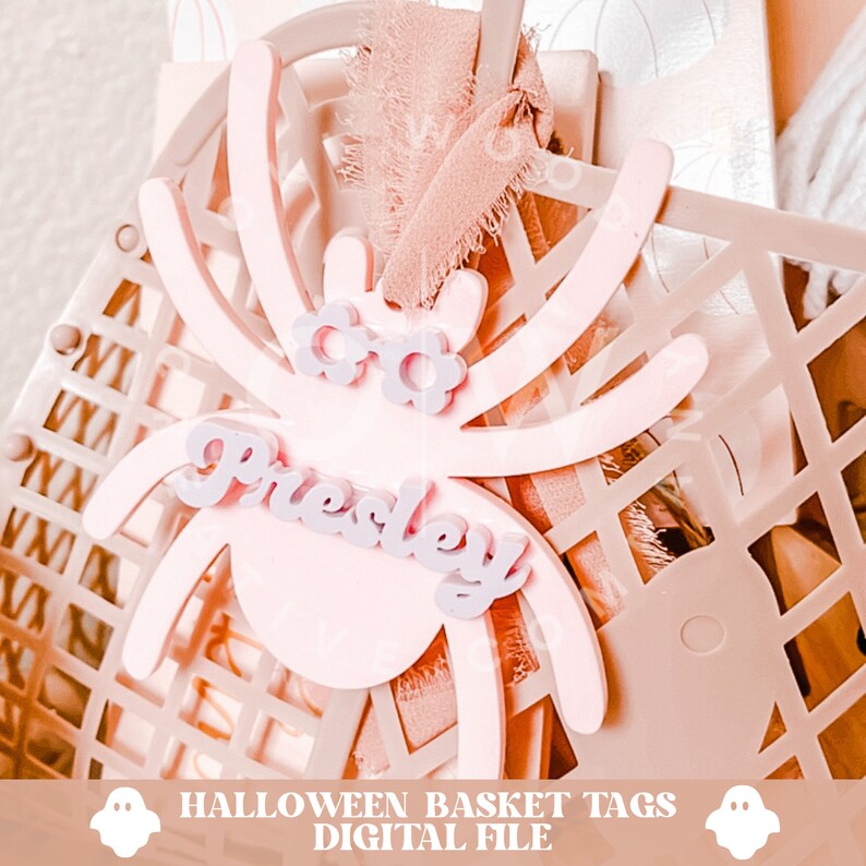 Pode incluir: Etiqueta de cesta de Halloween em forma de aranha rosa com o nome "Presley" em letras roxas.