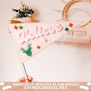 May include: A wooden pennant flag with the word "Believe" in pink letters. The flag is decorated with green and red stars and a green reindeer head.