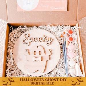 May include: A wooden craft kit with a round wooden base, a ghost cutout, and the word "Spooky" in cursive. The kit includes paint, brushes, and a small white cone. The text "Halloween Ghost DIY Digital File" is at the bottom of the image.