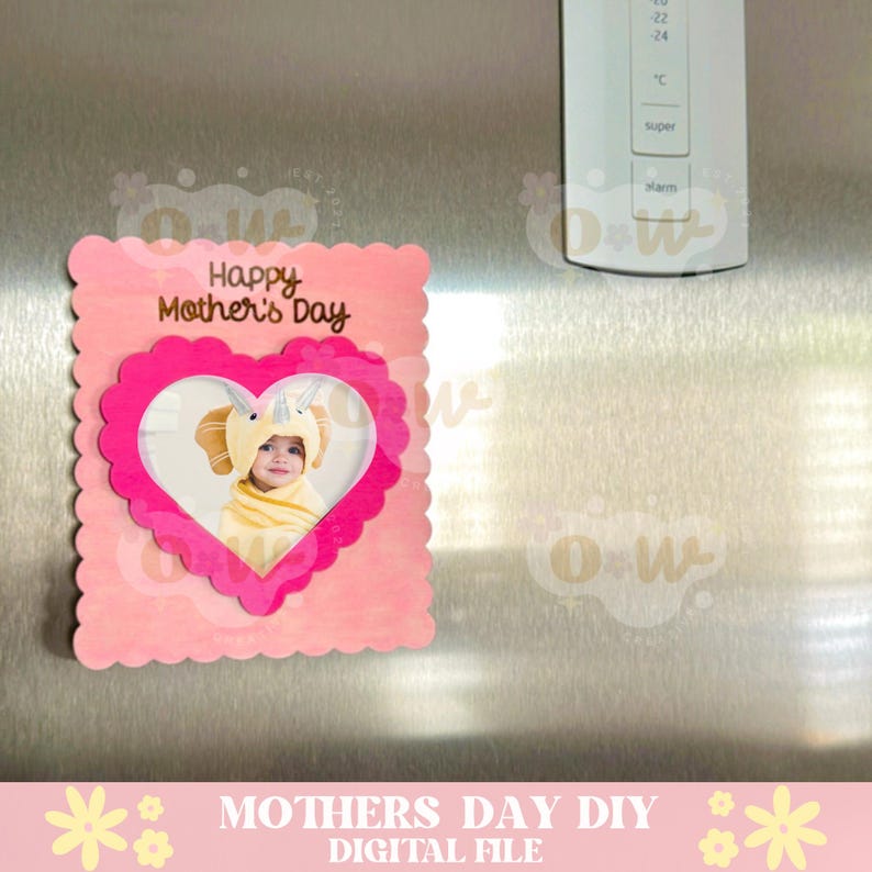 May include: A pink card with a scalloped edge and a heart-shaped photo frame. The card says "Happy Mother's Day" in gold lettering. A photo of a child wearing a yellow elephant costume is in the frame.