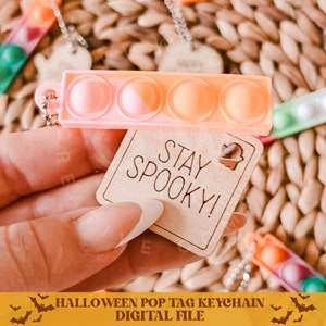 Op de afbeelding: Een roze en gele pop it sleutelhanger met een houten label waarop "Stay Spooky!" staat met een spookje. Halloween-sleutelhanger.