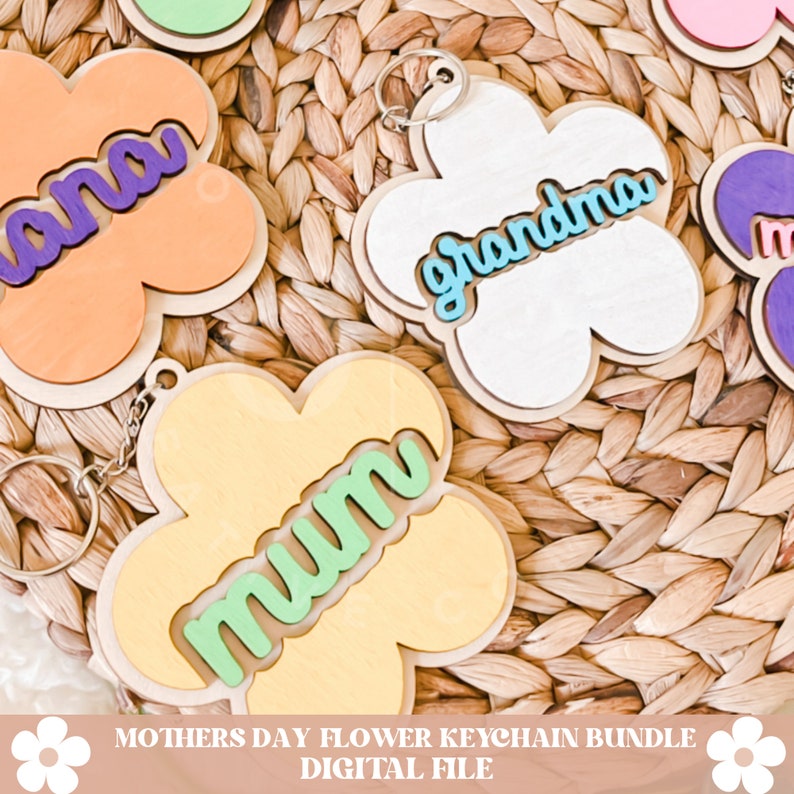 Puede incluir: Un conjunto de cinco llaveros de madera con forma de flor con diferentes fondos y textos de colores. Los llaveros dicen "Mum", "Grandma", "Nana" y dos m&aacute;s. Los llaveros est&aacute;n sobre un fondo de mimbre tejido.