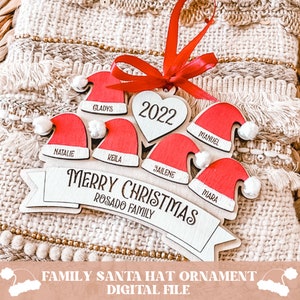 Puede incluir: Un adorno navide&ntilde;o de madera con forma de pancarta con un coraz&oacute;n y gorros de Pap&aacute; Noel. La pancarta dice "Merry Christmas Rosado Family" y el coraz&oacute;n tiene el a&ntilde;o "2022" en &eacute;l. Cada gorro de Pap&aacute; Noel tiene un nombre: Gladys, Keila, Jailene, Mara, Natalie y Manuel.