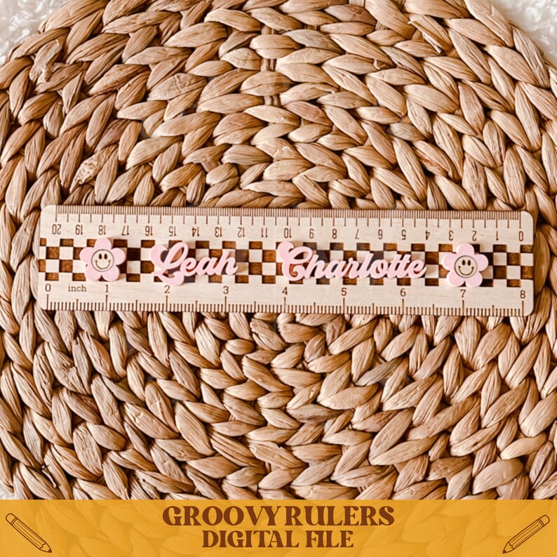 May include: A wooden ruler with a checkered pattern and pink smiley faces. The ruler is labeled with the names "Leah" and "Charlotte" and has inch markings.