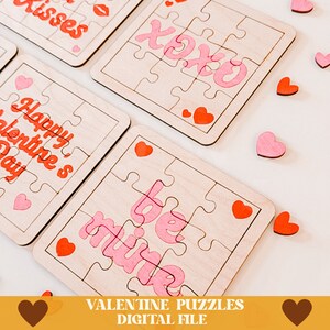 May include: Four wooden jigsaw puzzles with pink and red lettering on a white background. The puzzles feature the phrases "Happy Valentine's Day", "XOXO", "Kisses", and "Be Mine".