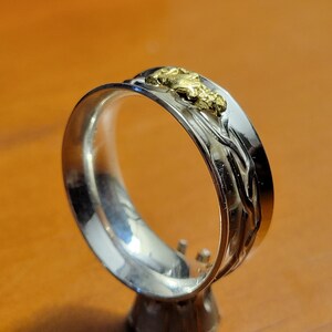 May include: A silver band with a textured design and a small piece of gold nugget embedded in the band.