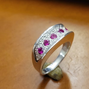 May include: A silver ring with a textured band and five pink gemstones set in a row.