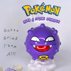 May include: A purple herb and spice grinder shaped like a cartoon character with a smiling face, white eyes, and red mouth. The grinder has a cylindrical handle and a small tool. The text "Gotta Grind Them All!" is also visible.