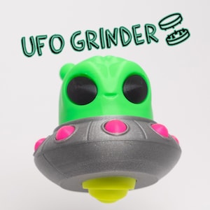May include: A green alien-shaped UFO grinder with pink accents and a silver base. The grinder has a yellow lid and the text "UFO GRINDER" is written above it.