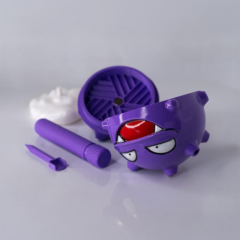May include: A purple, cartoon-style container with a red interior and white teeth and eyes. A purple cylinder, a small purple tool, a purple circular piece, and a white, cloud-shaped object are also present.