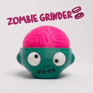 Peut inclure: Un moulin à herbes en forme de tête de zombie vert et rose avec le texte "ZOMBIE GRINDER" au-dessus.