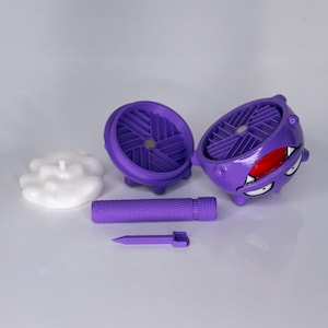 May include: A purple, spherical container with a cartoon face, open to reveal a fan-like interior. A white cloud-shaped object and a purple cylinder and spike are also present. The container has a red mouth and white eyes.