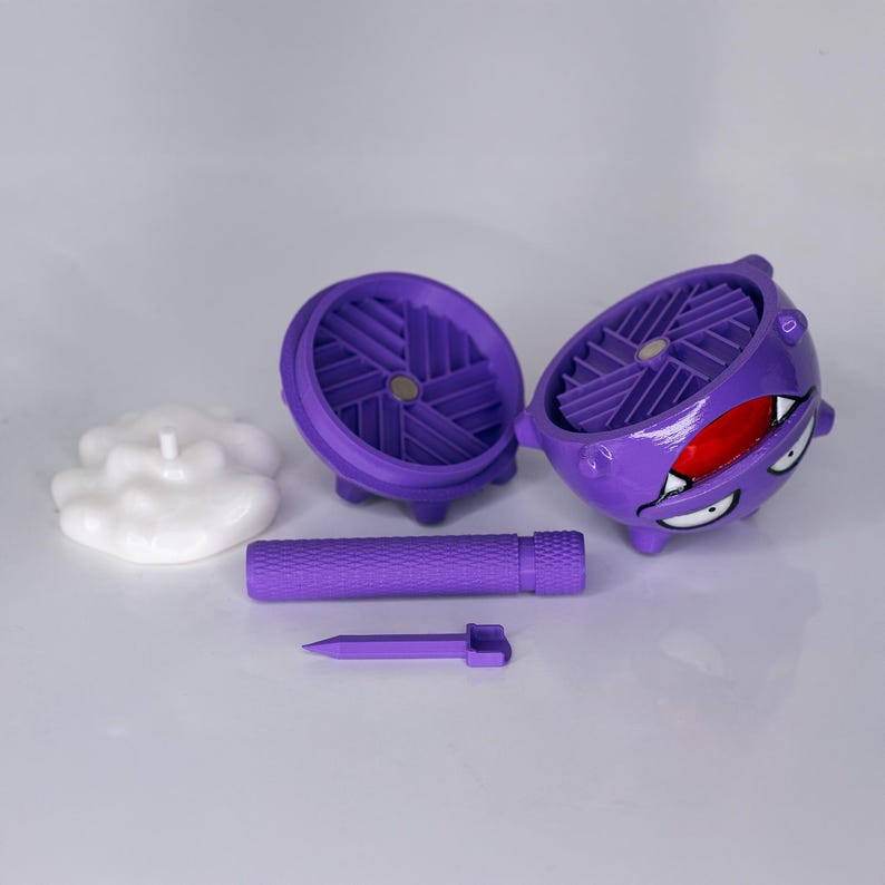 May include: A purple, spherical container with a cartoon face, open to reveal a fan-like interior. A white cloud-shaped object and a purple cylinder and spike are also present. The container has a red mouth and white eyes.