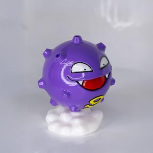 May include: A purple, spherical figure with a smiling face, white eyes, and a red mouth. The figure has small protrusions and sits atop a white cloud-shaped base. A yellow number 9 is visible on the figure.