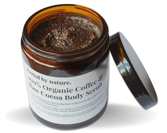 May include: A brown glass jar with a black lid filled with a dark brown coffee and cocoa body scrub. The jar has a white label with the text "Rooted by nature. 100% Organic Coffee & Raw Cocoa Body Scrub".