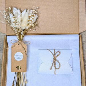 May include: A brown gift box containing a bouquet of dried flowers, a tag with the text "EVER + EDEN", and a white card tied with twine. The contents are arranged on white tissue paper.