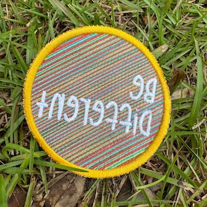 May include: A round, yellow-trimmed patch with a colorful striped background and the text "Digital 99" embroidered in white.