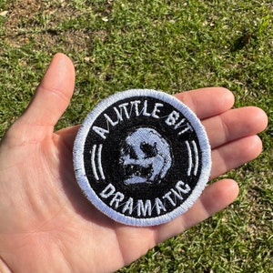 May include: A black and white embroidered patch with a skull and the text "A Little Bit Dramatic".