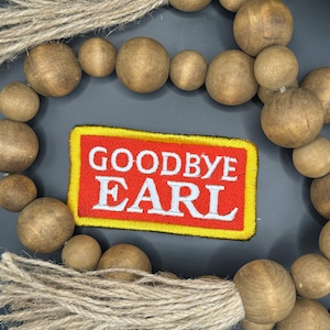 May include: A wooden bead garland with a red and yellow patch that says "Goodbye Earl" in white text. The garland has two tassels made of natural fiber.