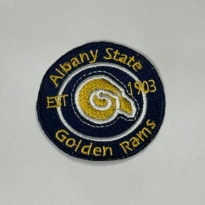 May include: A navy blue and gold embroidered patch with the words "Albany State" and "Golden Rams" around a gold ram's head logo. The text "EST 1903" is also included.
