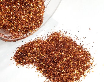 May include: A close-up of a jar of copper glitter. The glitter is spilling out of the jar and onto a white surface.