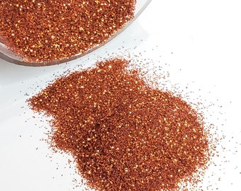 May include: A close-up of a pile of fine copper glitter, with a small amount spilling out of a clear jar.