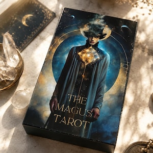 May include: A tarot card box with the words "THE MAGUS TAROT" in gold lettering. The box features an illustration of a figure in a long coat with a cosmic background. Other tarot cards and crystals are also visible.