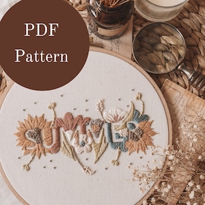 Peut inclure: Un modèle PDF pour un cerceau à broder avec le mot "SUMMER" brodé en fil coloré avec des accents floraux. Le cerceau est sur un tapis tissé avec des fleurs séchées et une loupe.