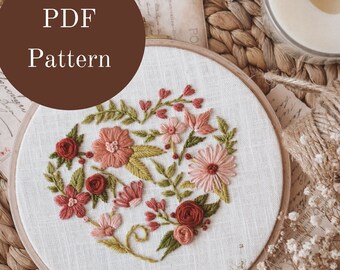 May include: A PDF pattern for a floral embroidery design. The design features a heart shape filled with pink, red, and green flowers. The pattern is displayed on a white embroidery hoop.