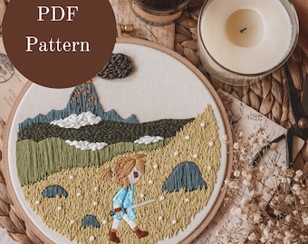 May include: A PDF pattern for an embroidery hoop featuring a girl with a sword standing in a field with a mountain in the background. The embroidery is done in shades of green, blue, and yellow.