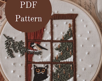 Puede incluir: Un patrón PDF para un aro de bordado que presenta una escena de ventana con un gato, un pájaro y un árbol de Navidad. La ventana está enmarcada en marrón y la escena se desarrolla sobre un fondo blanco con copos de nieve blancos.