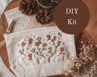 May include: DIY Kit for a small embroidered pouch with a floral design. The pouch is made of natural canvas fabric and features a zipper closure. The pouch is surrounded by pine cones, dried flowers, and a handwritten note.