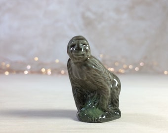 Könnte beinhalten: Eine Keramikfigur eines grauen Affen, der auf einem grünen Sockel sitzt. Der Affe hat einen verspielten Gesichtsausdruck.