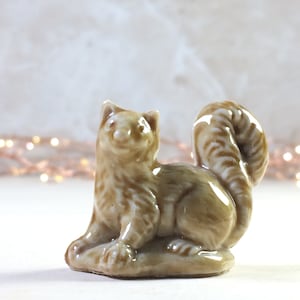 May include: A brown and white ceramic figurine of a squirrel sitting on its haunches with its tail curled up behind it.