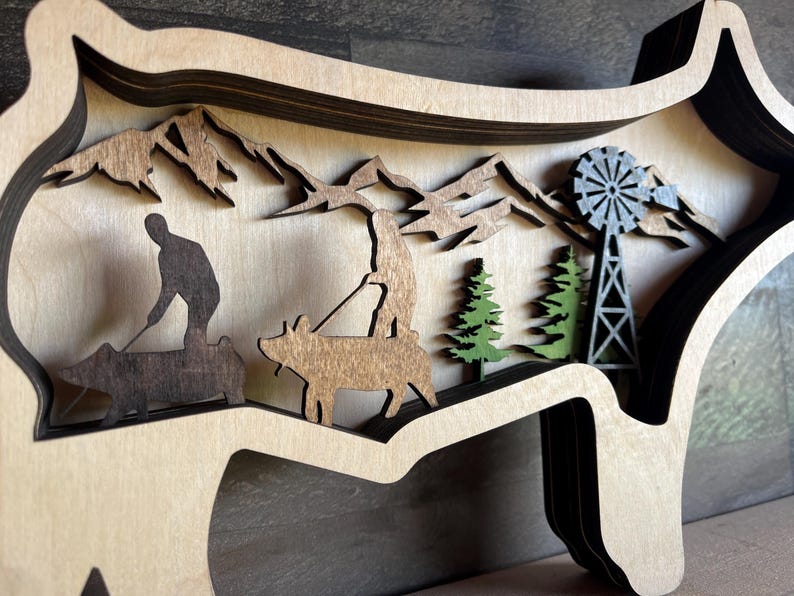 May include: A wooden wall decoration in the shape of a pig with a layered design. The pig is brown and features a silhouette of a person riding a pig, a windmill, and trees.