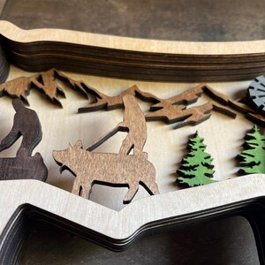 May include: A layered wooden wall art piece depicting a rural scene with a pig, two figures, trees, and a windmill. The piece is made of multiple layers of wood, creating a 3D effect.