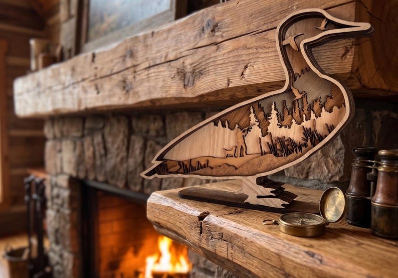 May include: A multi-layered wooden duck silhouette featuring a laser-cut forest landscape with pine trees and a small bird in flight. The sculpture is crafted from light and dark wood tones, creating a depth effect within the duck's body shape.