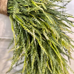 K&ouml;nnte beinhalten: Nahaufnahme eines B&uuml;ndels k&uuml;nstlichen Gr&uuml;ns, mit langen, schlanken Bl&auml;ttern in Gr&uuml;n- und Gelbt&ouml;nen. Die Bl&auml;tter sind mit einem dicken, naturfarbenen Bindfaden zusammengebunden, wodurch ein rustikales und strukturiertes Aussehen entsteht. Ideal f&uuml;r die Heimdekoration.